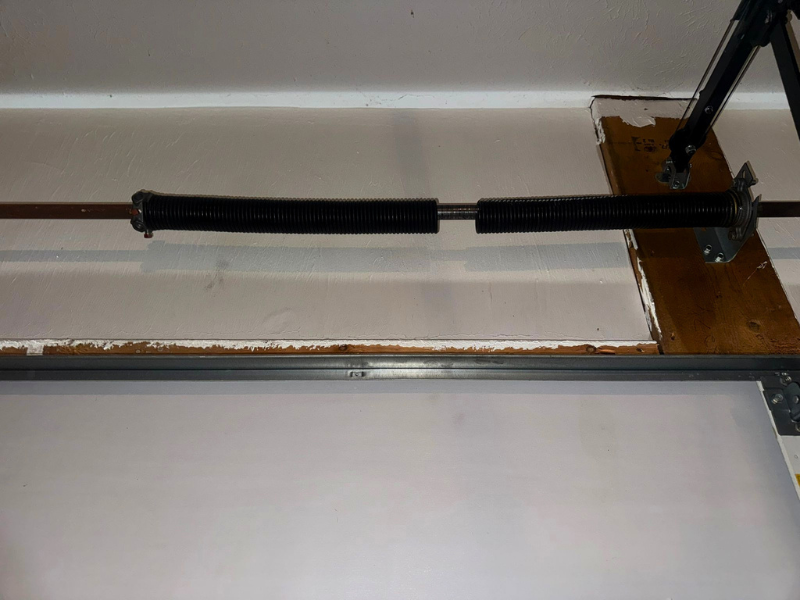 Worn cable and drum hardware on a residential garage door, similar to the wound cable that guides a garage door's lifting force